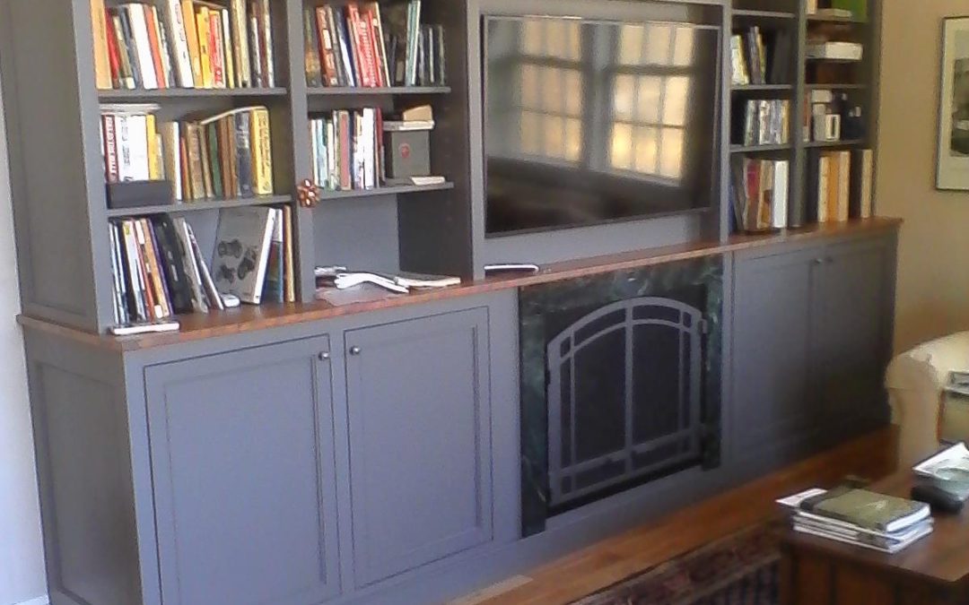 A cherry tabletop seperates lower storage cabinets and a gas fireplace from the television and breakfront bookcase above.