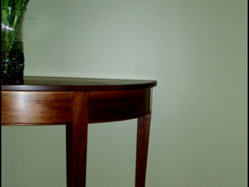 Walnut demilune table with curved and tapered legs.
