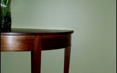 Walnut demilune table with curved and tapered legs.